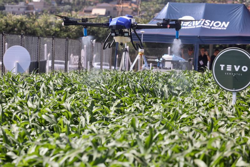 Spray drone hovering over a green crop plot during an agricultural field day
